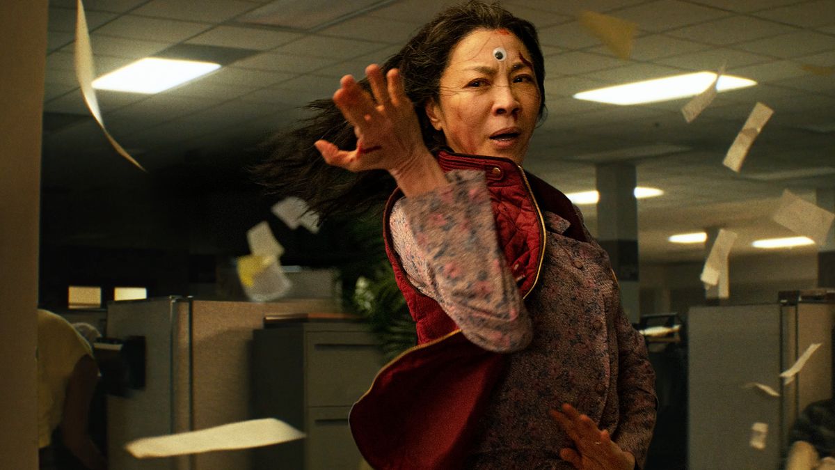 A bloodied Michelle Yeoh with a googly eye glued to her forehead strikes a martial arts pose in Everything Everywhere All at Once