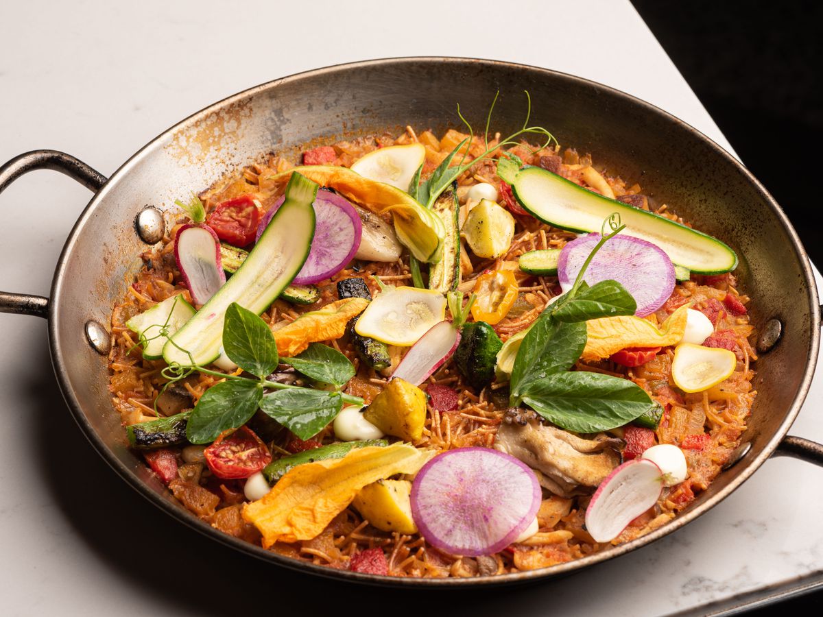 A paella pan with Spanish rice and topped with lots of colorful vegetables.