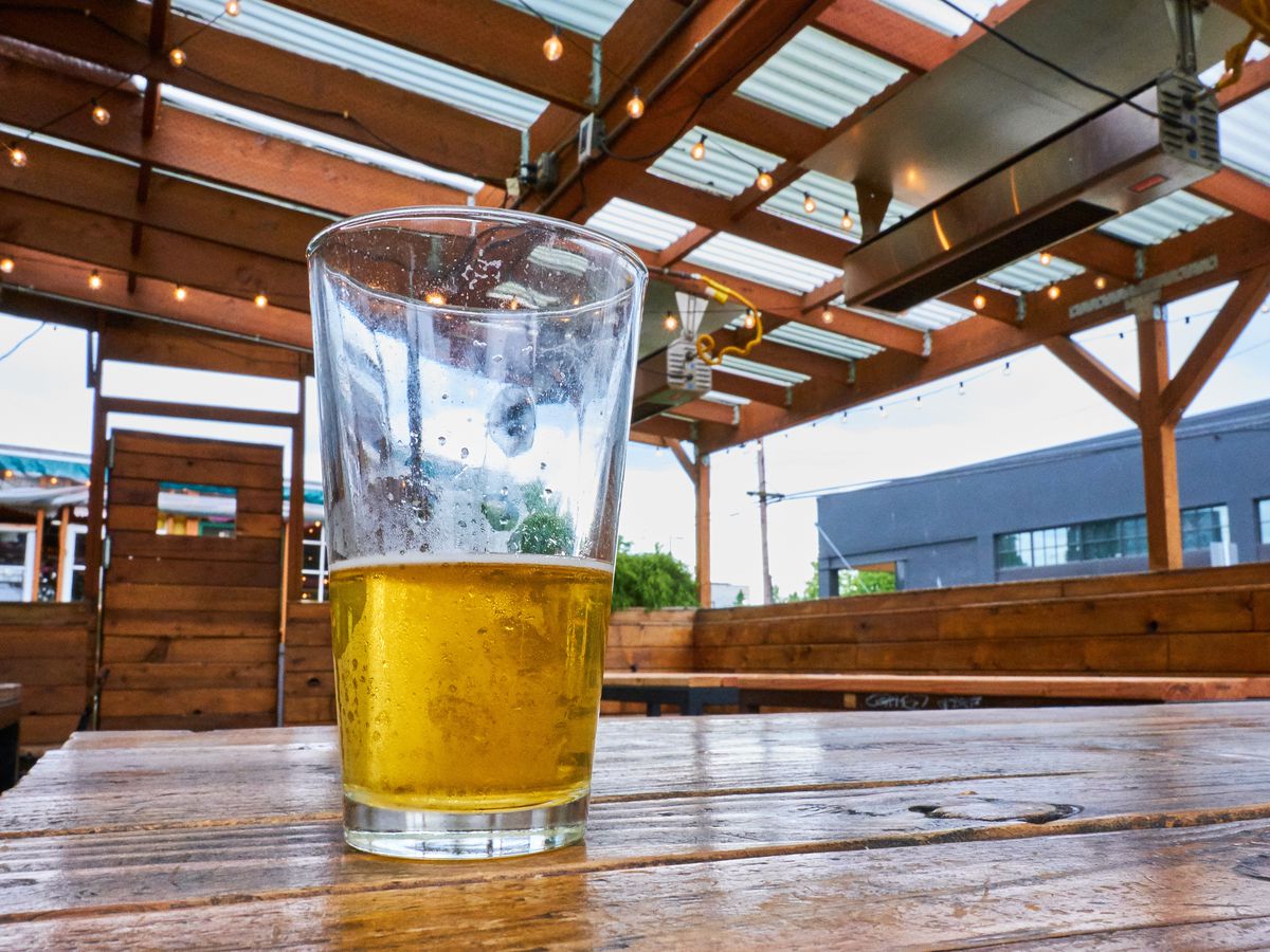 A half-empty pint of beer sitting on a wooden table under a corrugated patio roof.