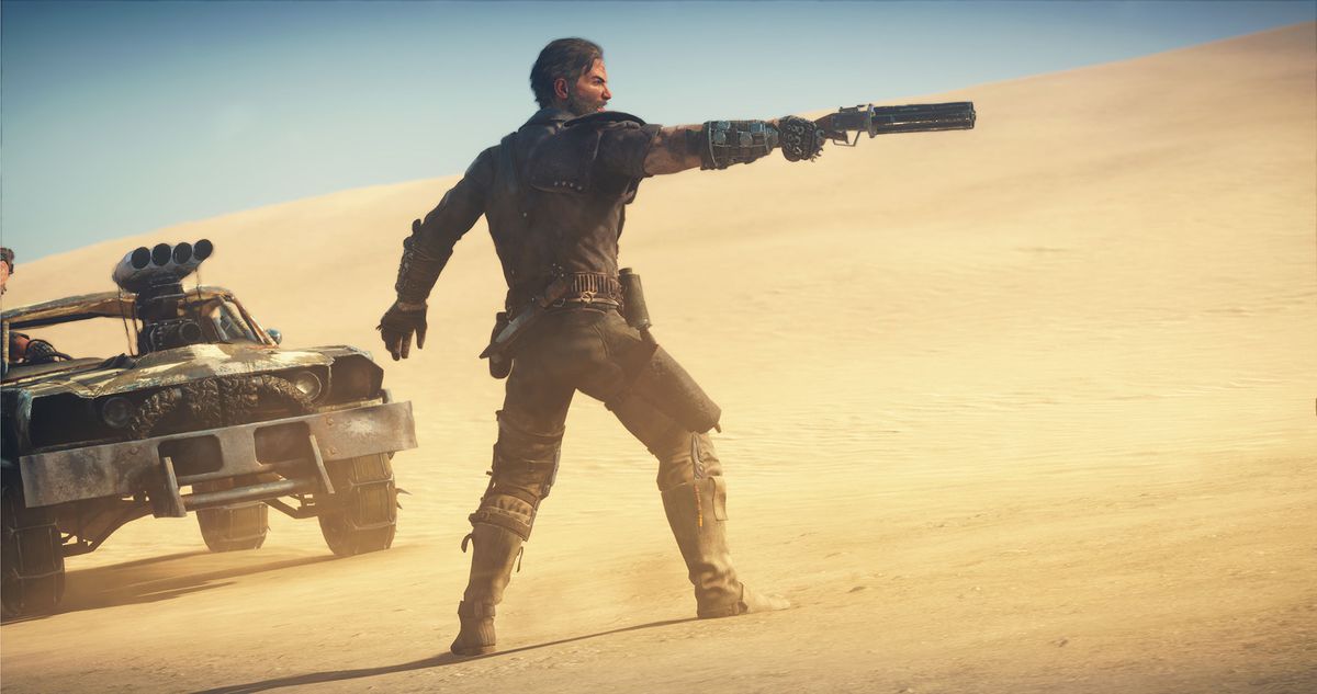 A man points a gun to the right in a desert landscape in Mad Max