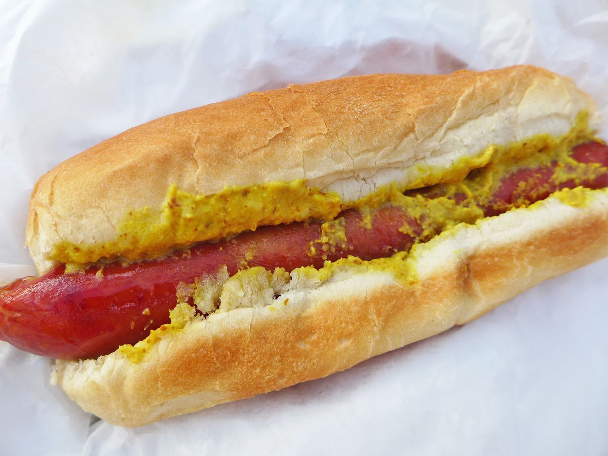 Hot dog on a long bun slathered with yellow mustard.