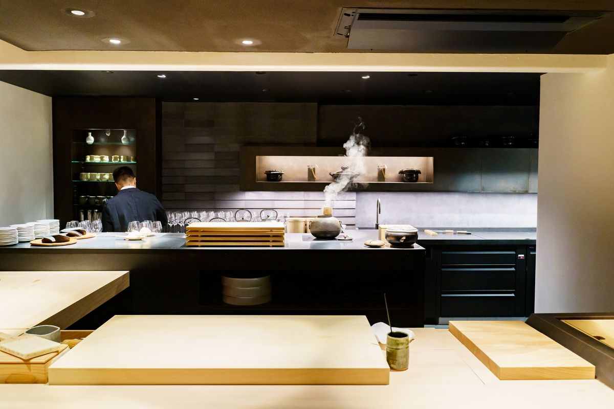 A worker in black is visible behind a light wooden sushi counter that appears to be underground.