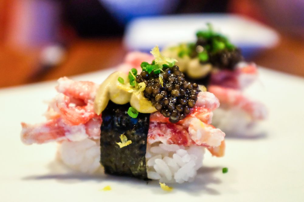 Several pieces of lobster sushi topped with caviar sit on a white plate.