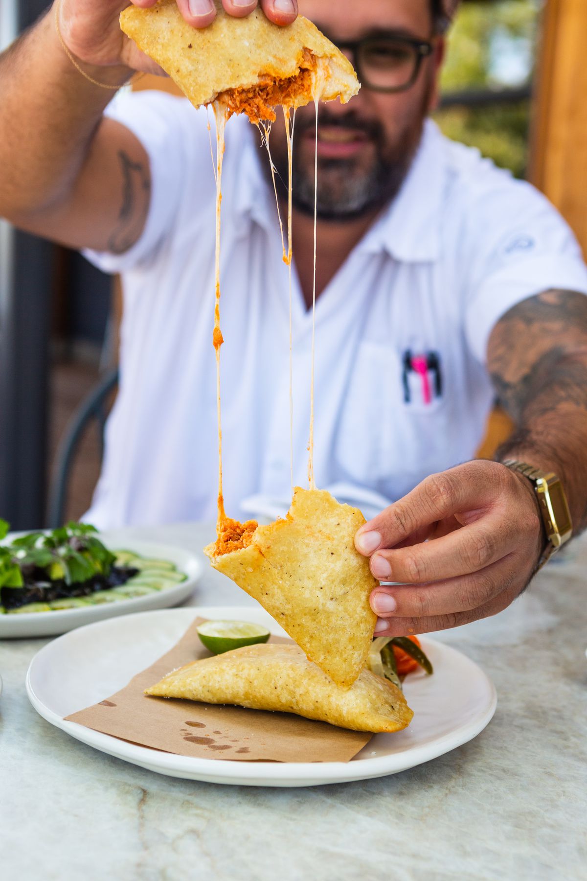 A man with a gold watch pulling an empanada apart with cheese between the two halves.