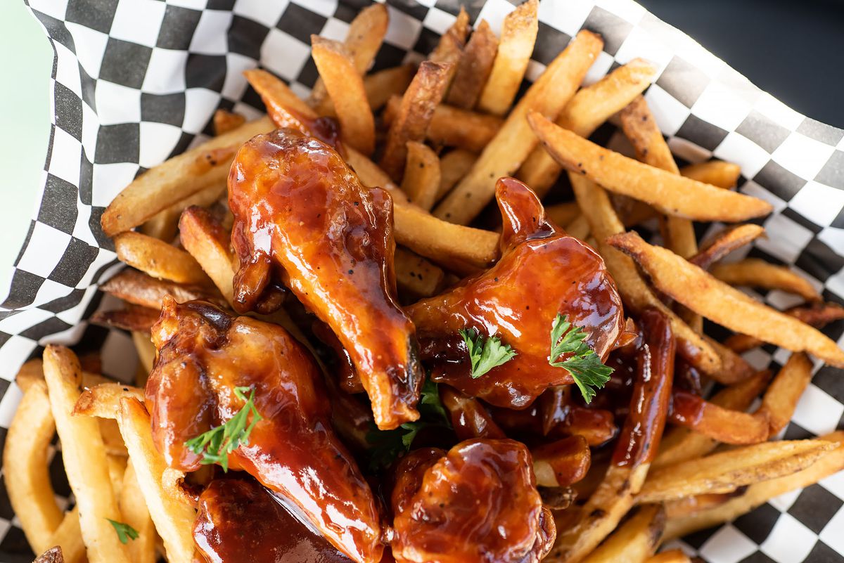 Barbecue chicken wings with fries on a checkered basket.
