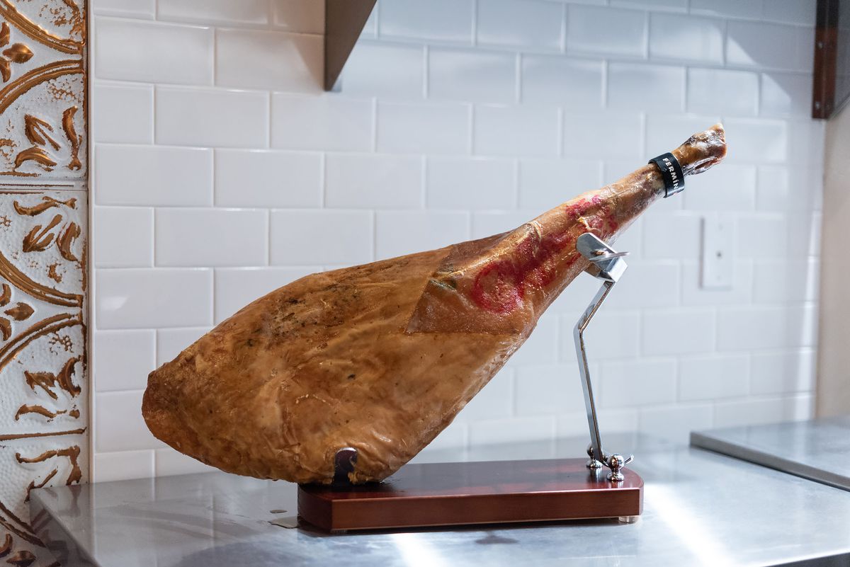A leg of jamon on a stand at a daytime restaurant.