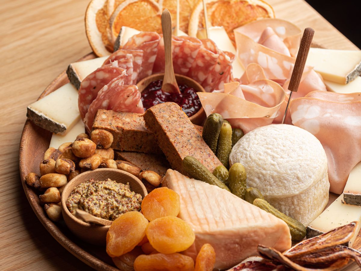 A round wooden board of meat and cheese with a collection of jams and spreads as well.