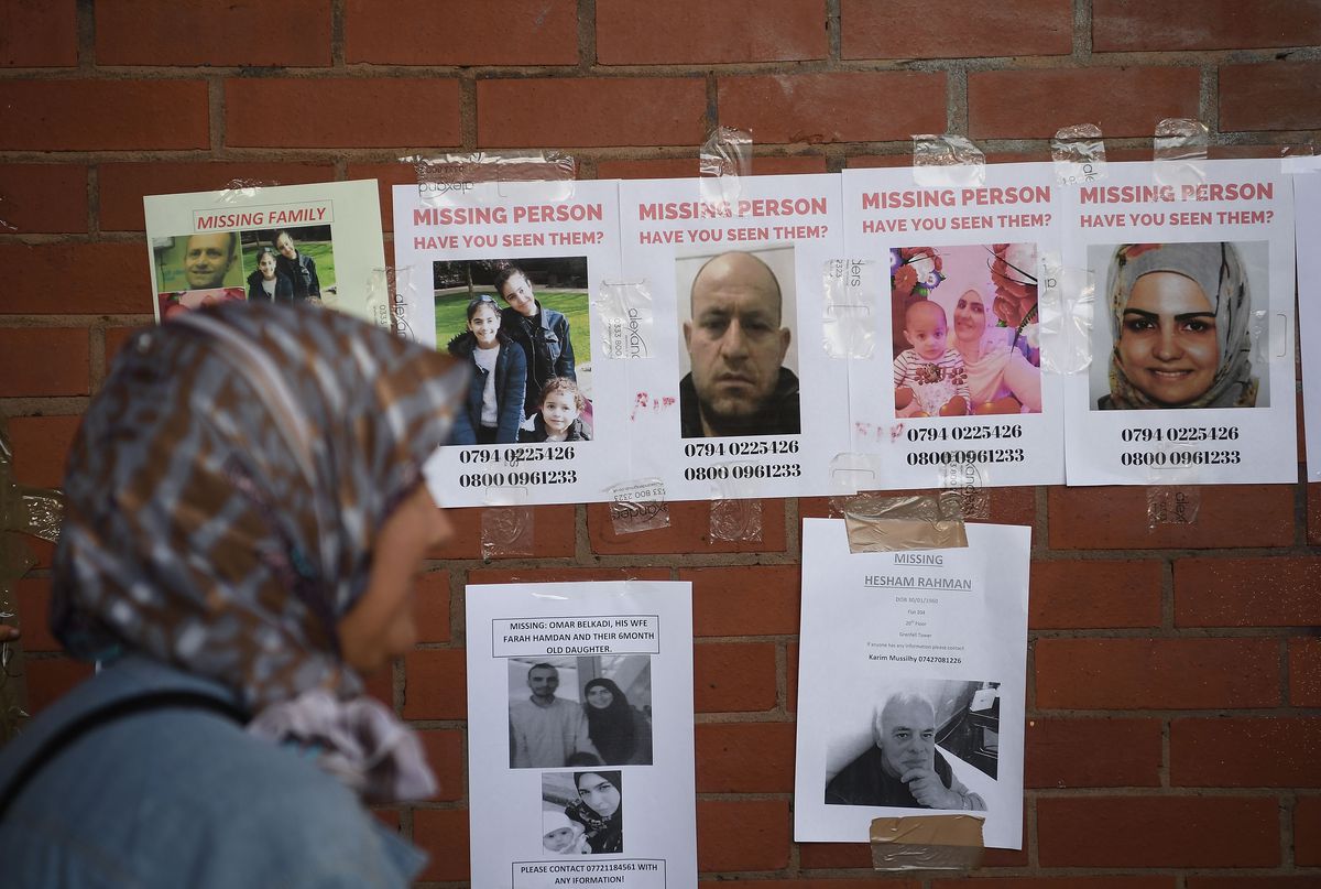 A woman wearing a headscarf looks at missing person photos posted on a brick wall