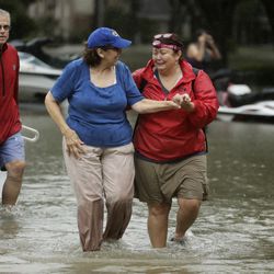 Julie Rios, left, walks out of their flooded neighborhood with newly-met neighbor Gina Delber, right, as they evacuate their homes that are inundated by floodwaters from Tropical Storm Harvey on Monday, Aug. 28, 2017, in Houston, Texas.