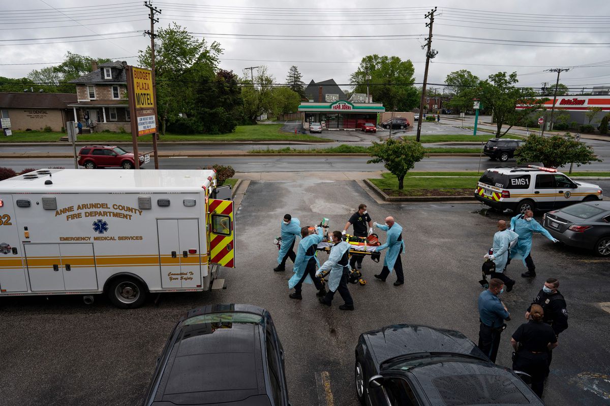 Firefighters and paramedics wheel a patient to an ambulance in a parking lot.