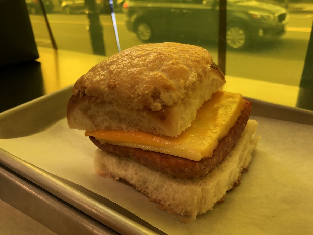 A sandwich with square cuts of spam, egg, and yellow cheese placed between two tall, fluffy buns.