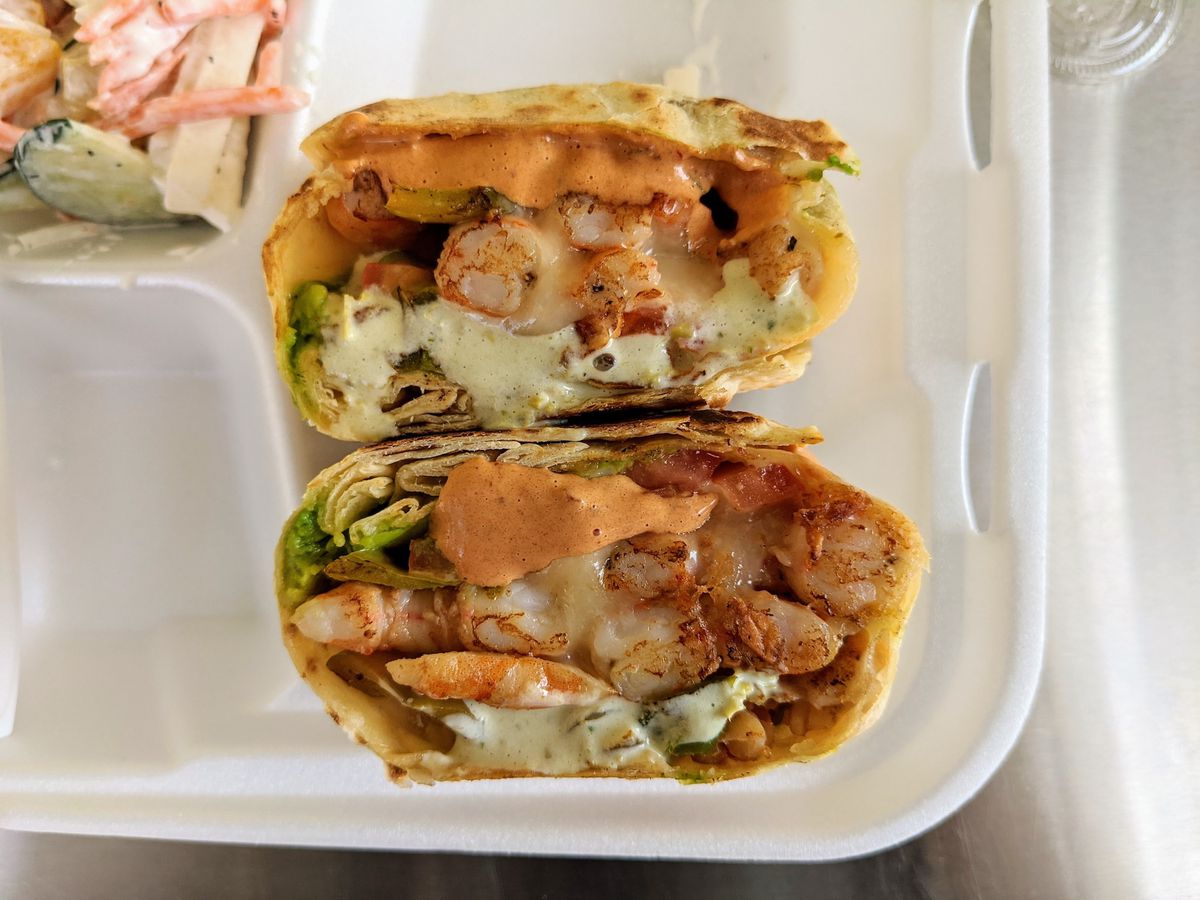 A shrimp burrito shown cut on the inside while sitting in a styrofoam container.