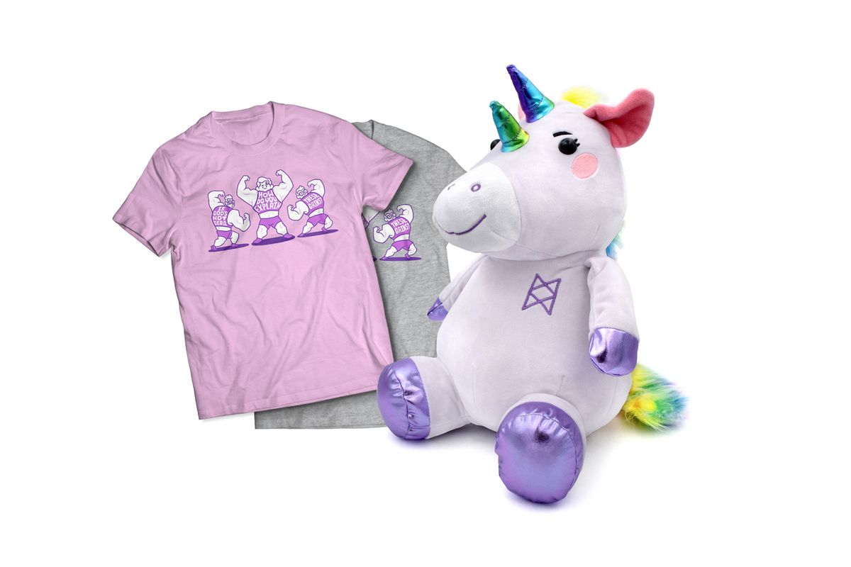 The August McElroy merch items. On the left are two shirts with buff McElroy brothers. Their shirts say, “If God’s not dead, how do you explain these gains?” The shirt in the front is purple. The shirt behind it is grey. To the right of the shirts is a Garyl plushie. His body is purple with pink cheeks. He has two rainbow horns and purple hooves. His mane and tail are rainbow faux fur. He has the B.O.B. symbol embroidered on his chest. There is a tag hanging from his ear that says, “TAZ”. 
