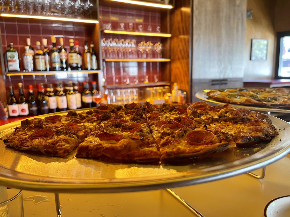 Nonno’s tavern-style Meat Head pizza topped with cheese, sausage, pepperoni, and capicola, sits on a silver tray at the bar.