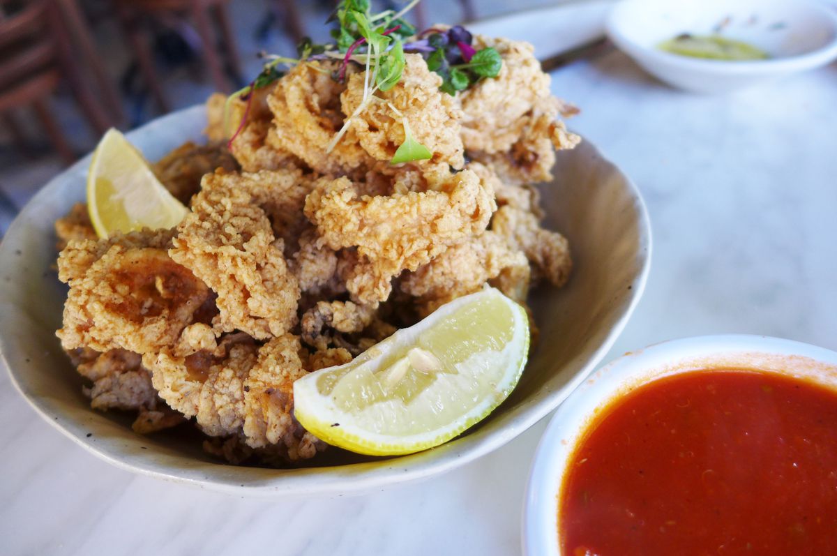 A plate of fried squid with lemon wedges and tomato sauce on the side.