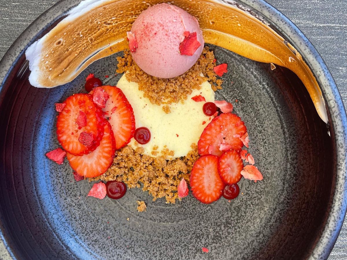 A deconstructed strawberry lemon meringue pie at Tableau, served on a black plate with scoops of ice cream and strawberry slices.