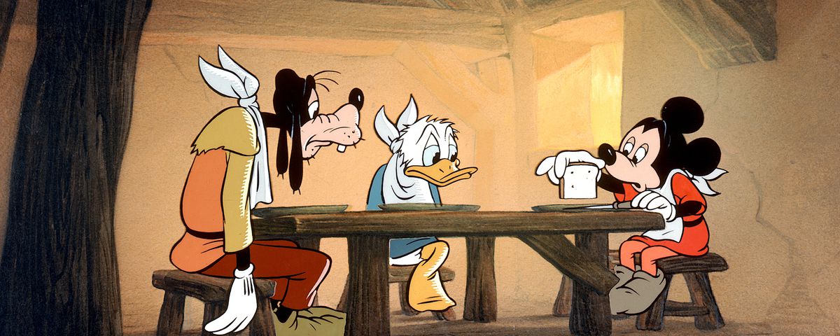 In a scene from the 1947 short Mickey and the Beanstalk, Goofy, Donald Duck, and Mickey Mouse slump hungrily over a wooden table in a bare room, wearing napkins around their necks and getting ready to split a single bean three ways