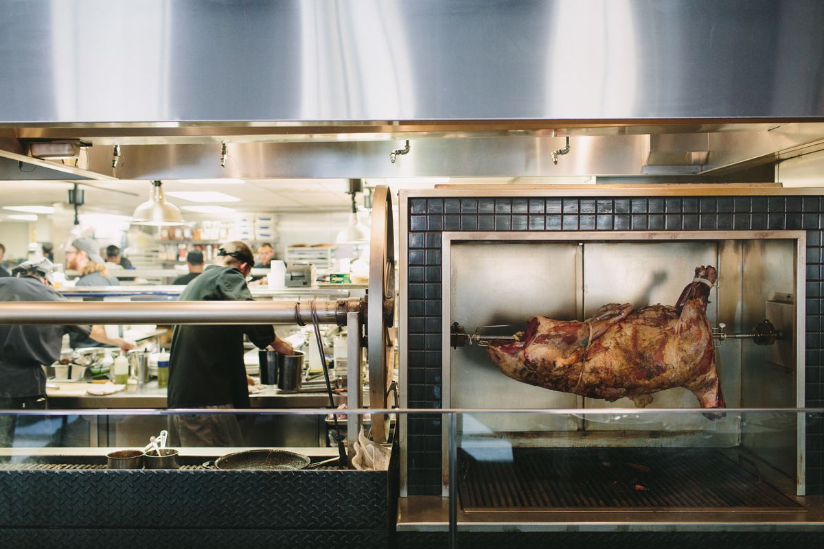 A pig roasting on a spit surrounded by black tile in front of an open kitchen at Roast in Detroit. 