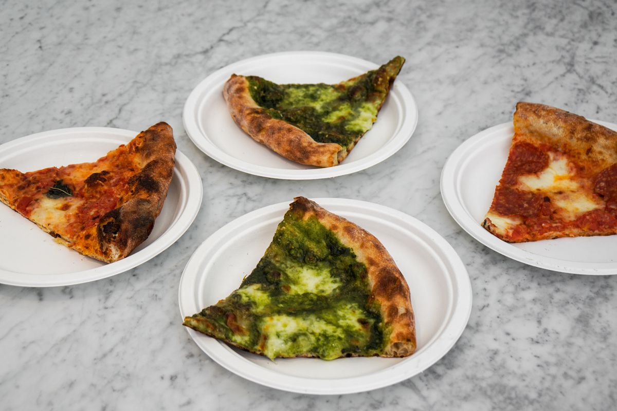 A marble countertop filled with pizza slices on paper plates at Pane Bianco.