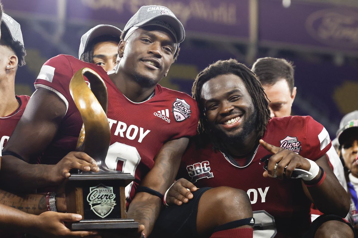 ORLANDO, FLORIDA - DECEMBER 16: RaJae’ Johnson #0 and Carlton Martial #2 of the Troy Trojans hold the trophy after defeating the UTSA Roadrunners by a score of 18 to 12 to win the Duluth Trading Cure Bowl at Exploria Stadium on December 16, 2022 in Orlando, Florida.