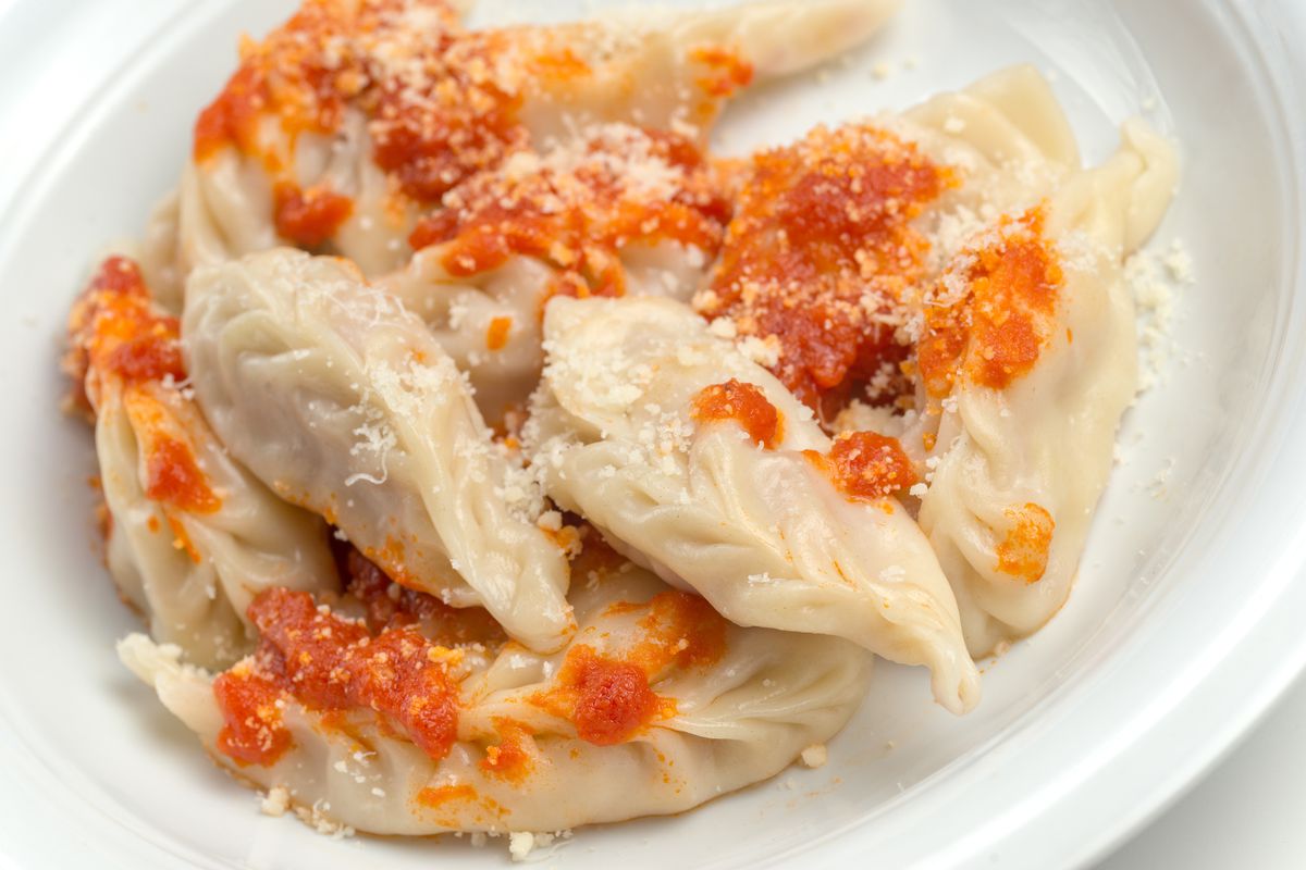 Plump dumpling-like culugriones scattered with tomatoes and cheese