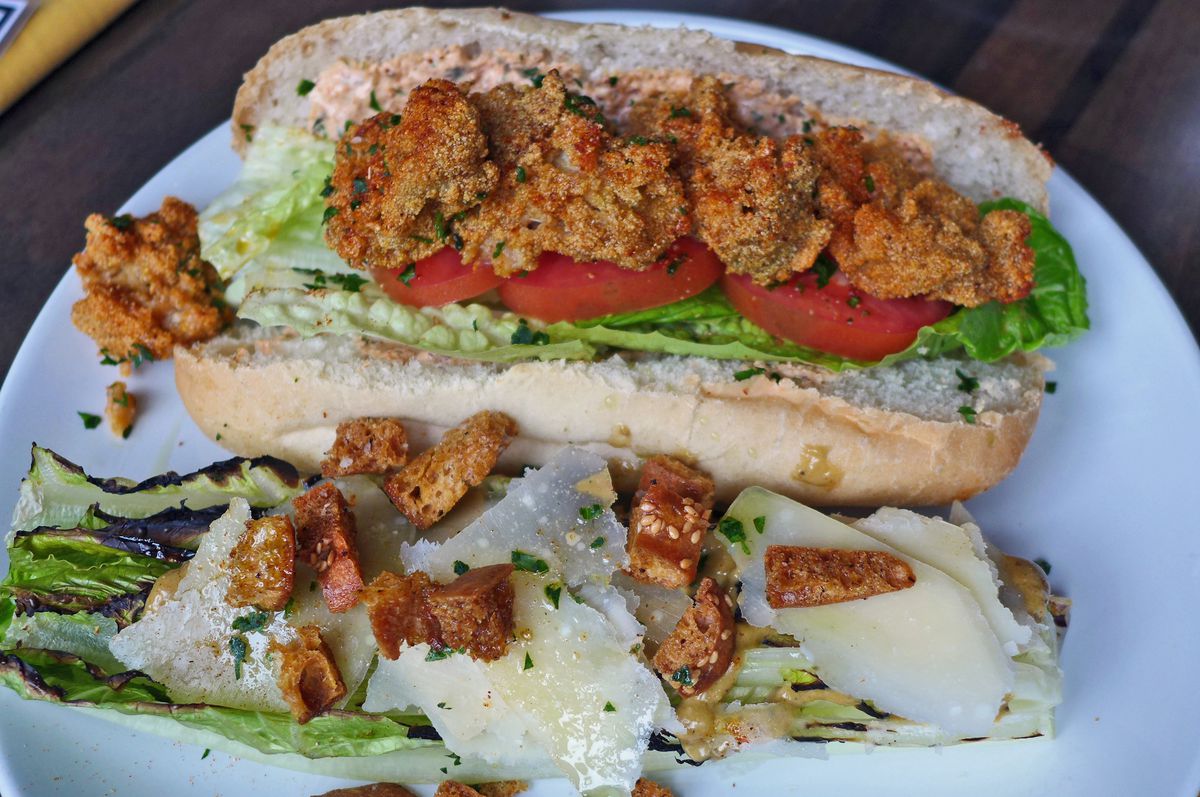 A baguette sandwich opened up to show five fried oysters.