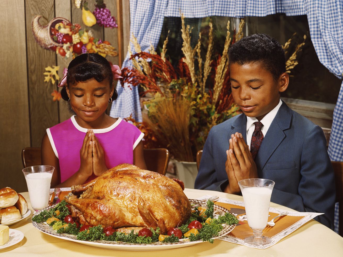 Image of the 1970s of a boy and girl saying grace at the dinner table with turkey in front of them.