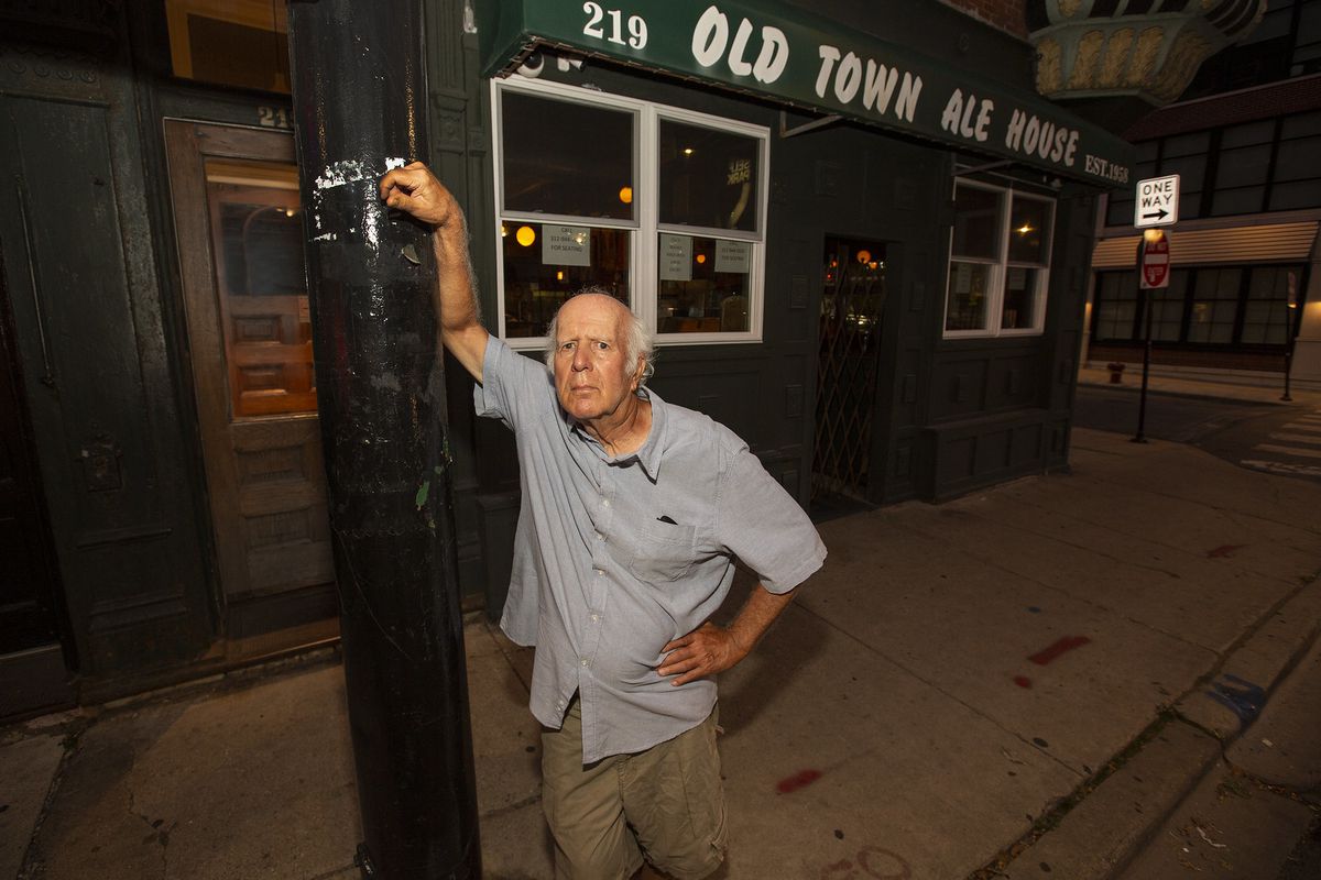 A character leaning on a light pole in front of a bar.