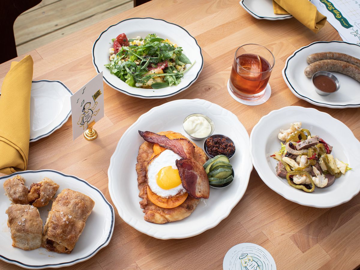 A spread of food including salad, pepperoni balls, and fried pork with an egg displayed in white porcelain dishes on top of a brown wooden table