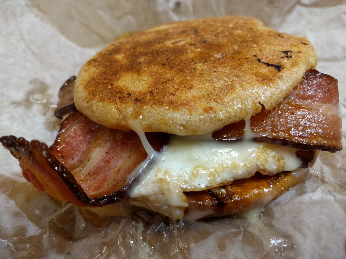 A mega-greasy breakfast melt with egg, two slices of bacon, and fontina cheese on a pressed English muffin