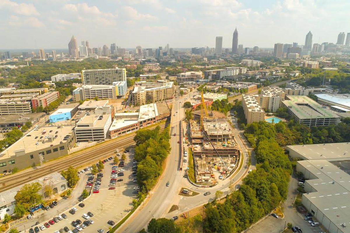 An aerial of a construction site at bottom with many high rise buildings in the distance.