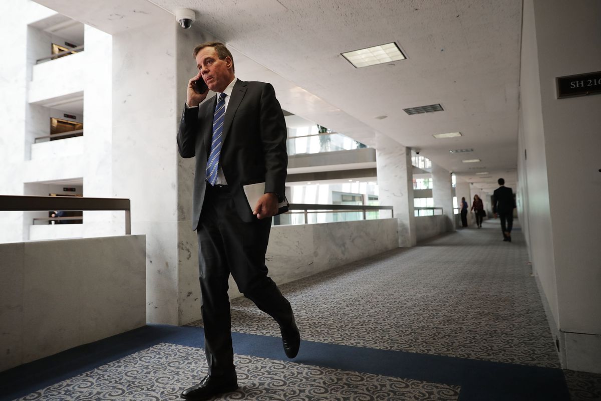 Democratic Senator Mark Warner walks down a hall talking on his phone.