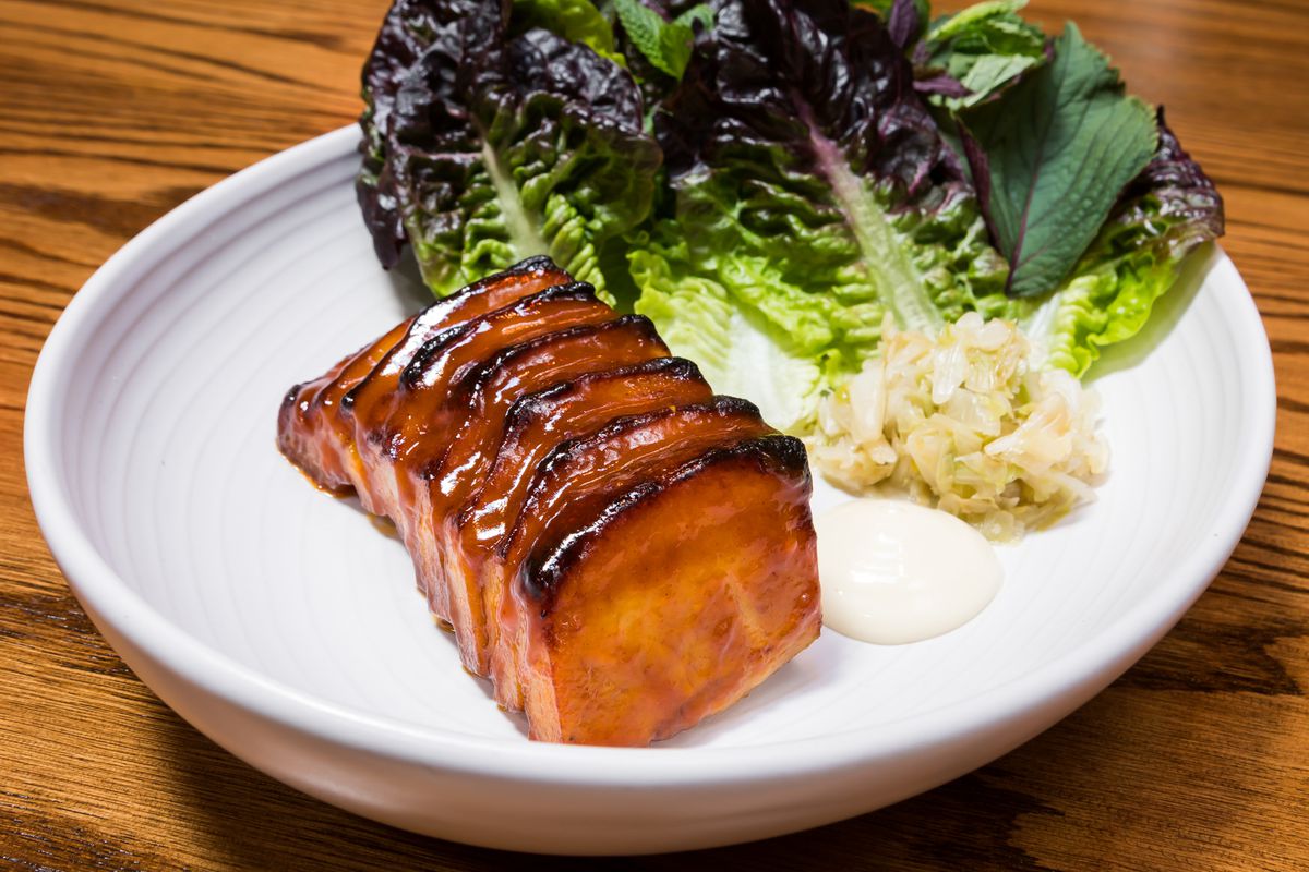 Sliced pork belly on plate with leaves of lettuce and herbs.