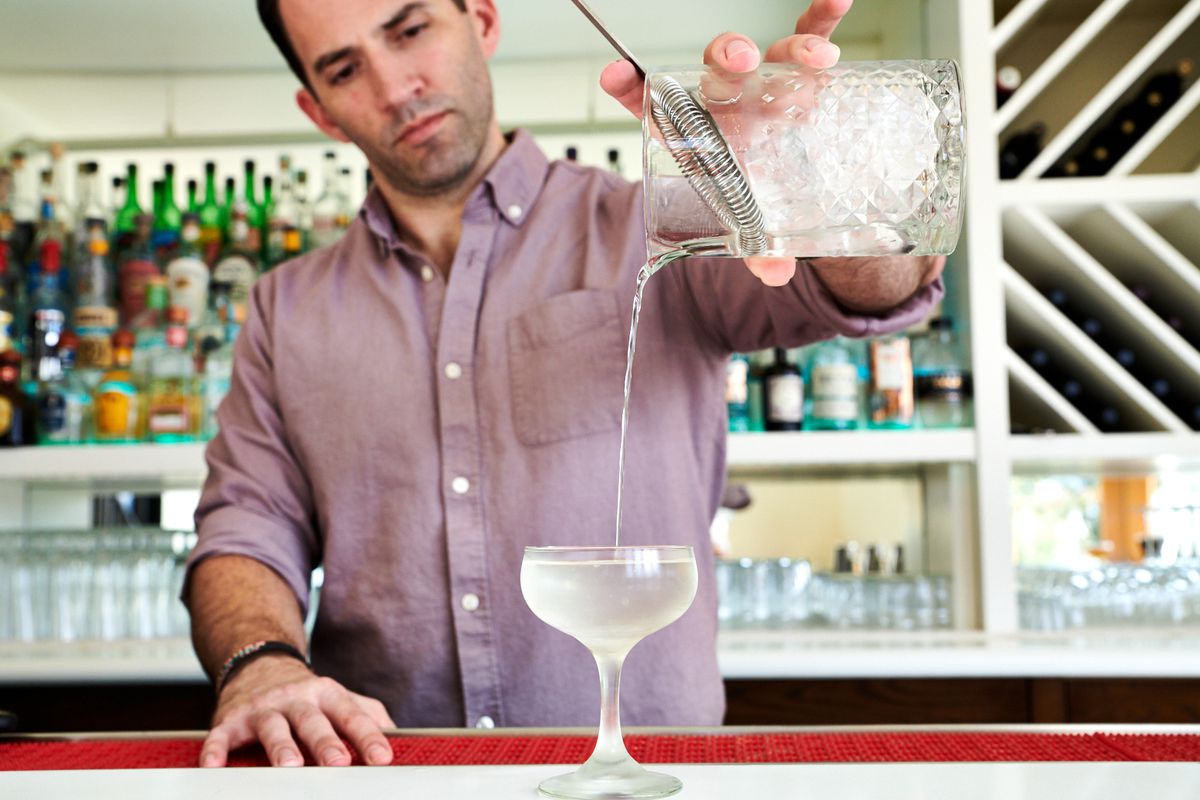 Ricky Gomez pours a martini into a coupe glass behind the white-and-turquoise bar at Palomar