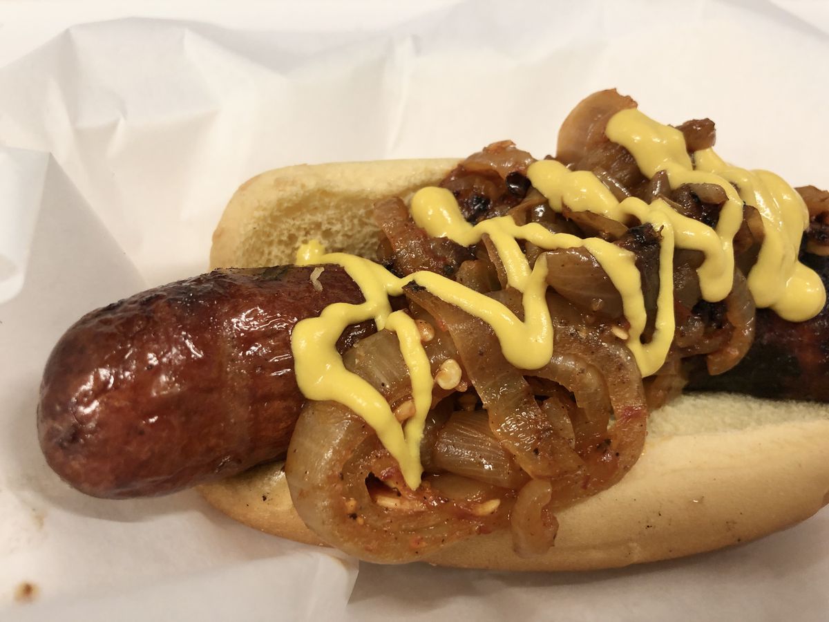 A sausage drizzled with mustard and onions on a bun.