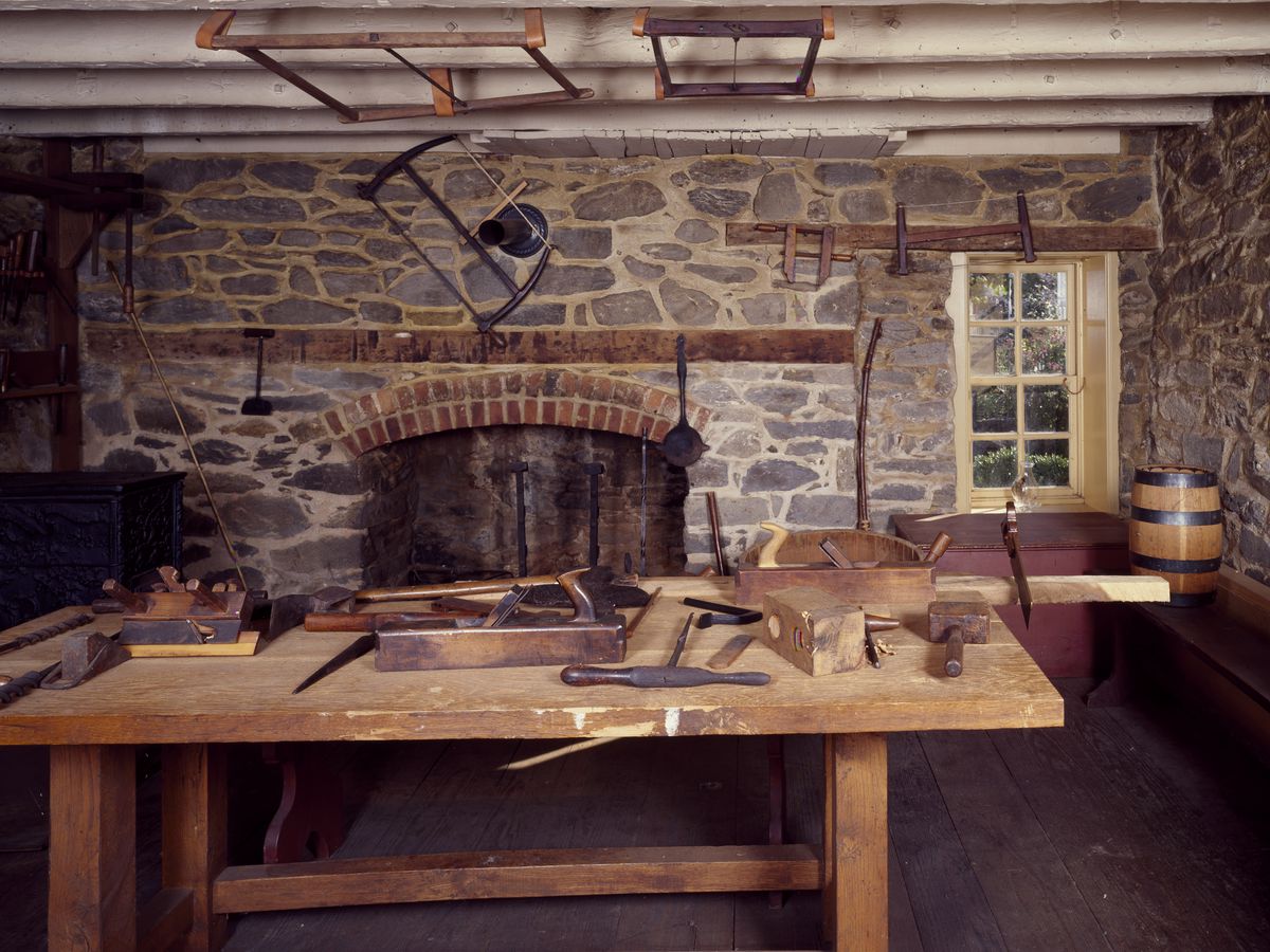 The interior of a stone house, outfitted with a wood work table and various tools.