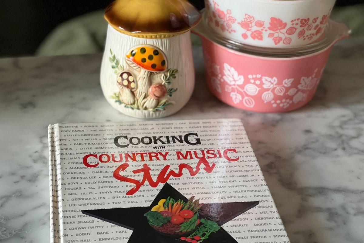 “Cooking With Country Music Stars” book on a marbletop counter with pink Pyrex containers.