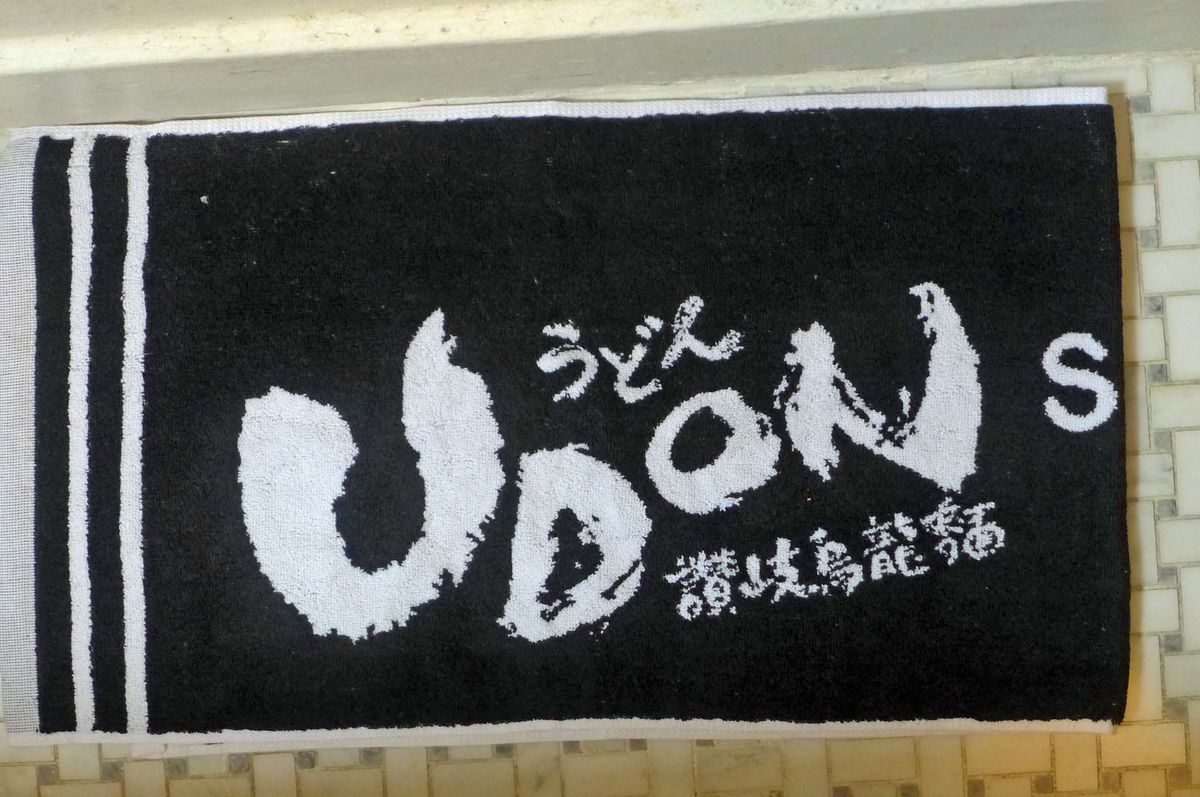A black towel with Udon scrawled in white on a black background.