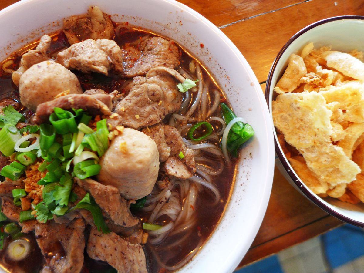 A bowl of dark broth is jammed with pork and pork balls, with a bowl of crunchy pig skin on the side.