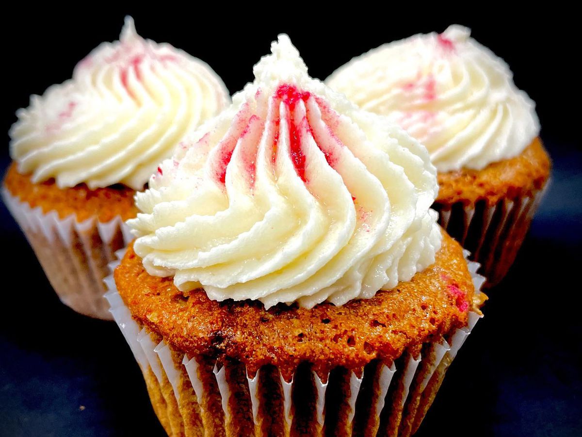 Three cupcakes with white frosting with pink spots.