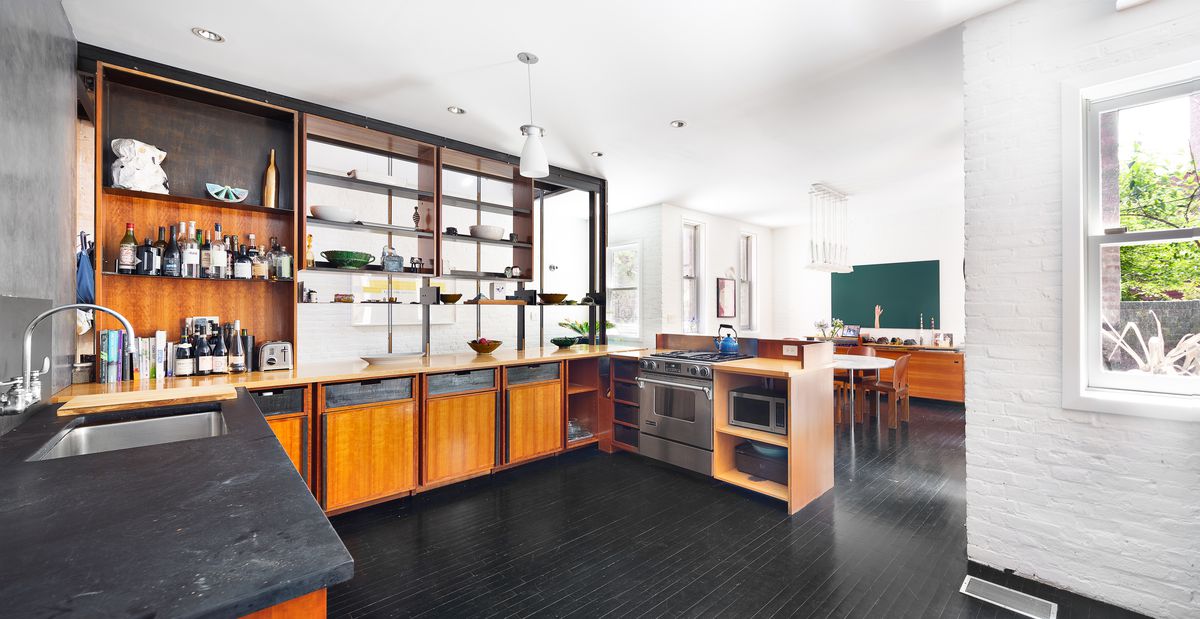 A kitchen with dark hardwood floors, white exposed brick, and wood cabinetry.