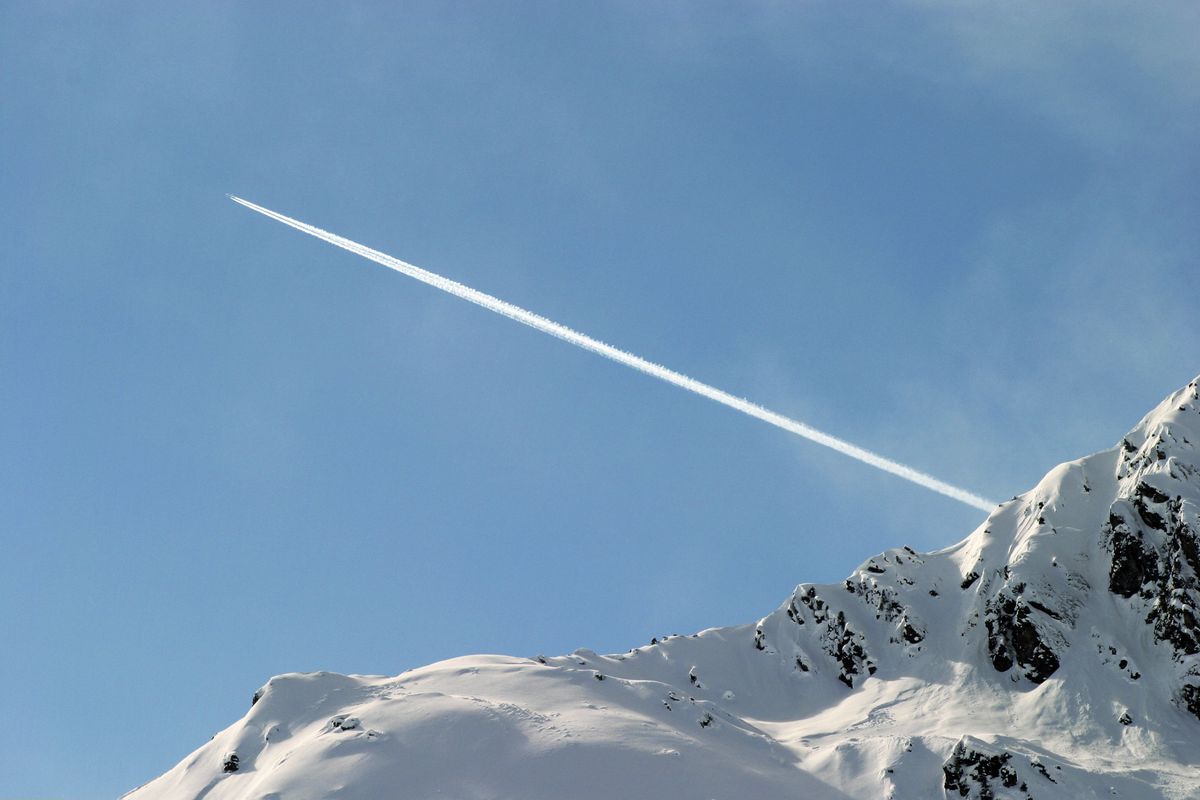 Flugzeug mit Kondenzstreifen ueber den Alpen