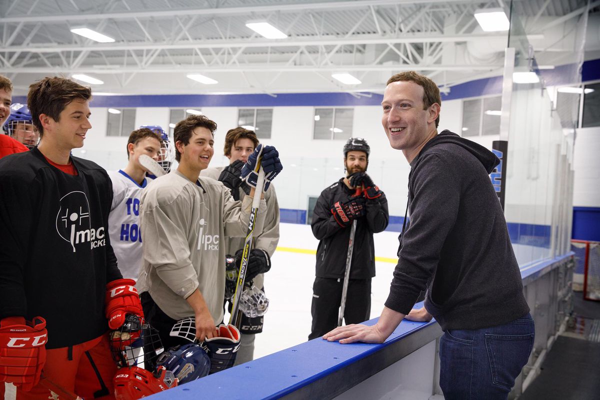 Facebook CEO Mark Zuckerberg leans on the wall around an indoor hockey rink and talks with hockey players.