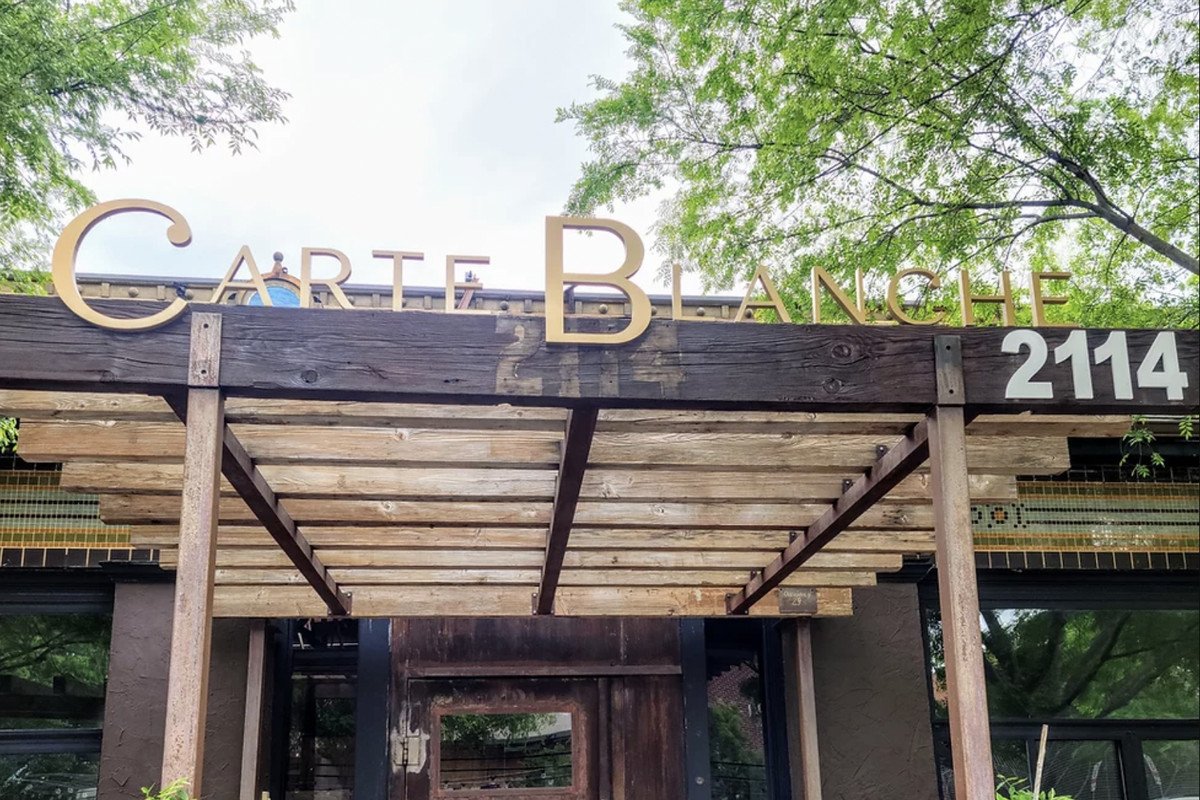 The exterior of Carte Blanche is on Lowest Greenville in Dallas with a wooden sign posted on a pergola.
