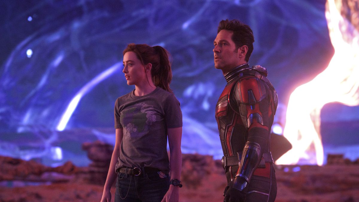 (L-R): Kathryn Newton as Cassandra “Cassie” Lang and Paul Rudd as Scott Lang/Ant-Man in Ant-Man and the Wasp: Quantumania. Cassie is in jeans and a t-shirt, while Scott is wearing his Ant-Man costume with the helmet off. They stand stunned on an alien vista with swirling skies.