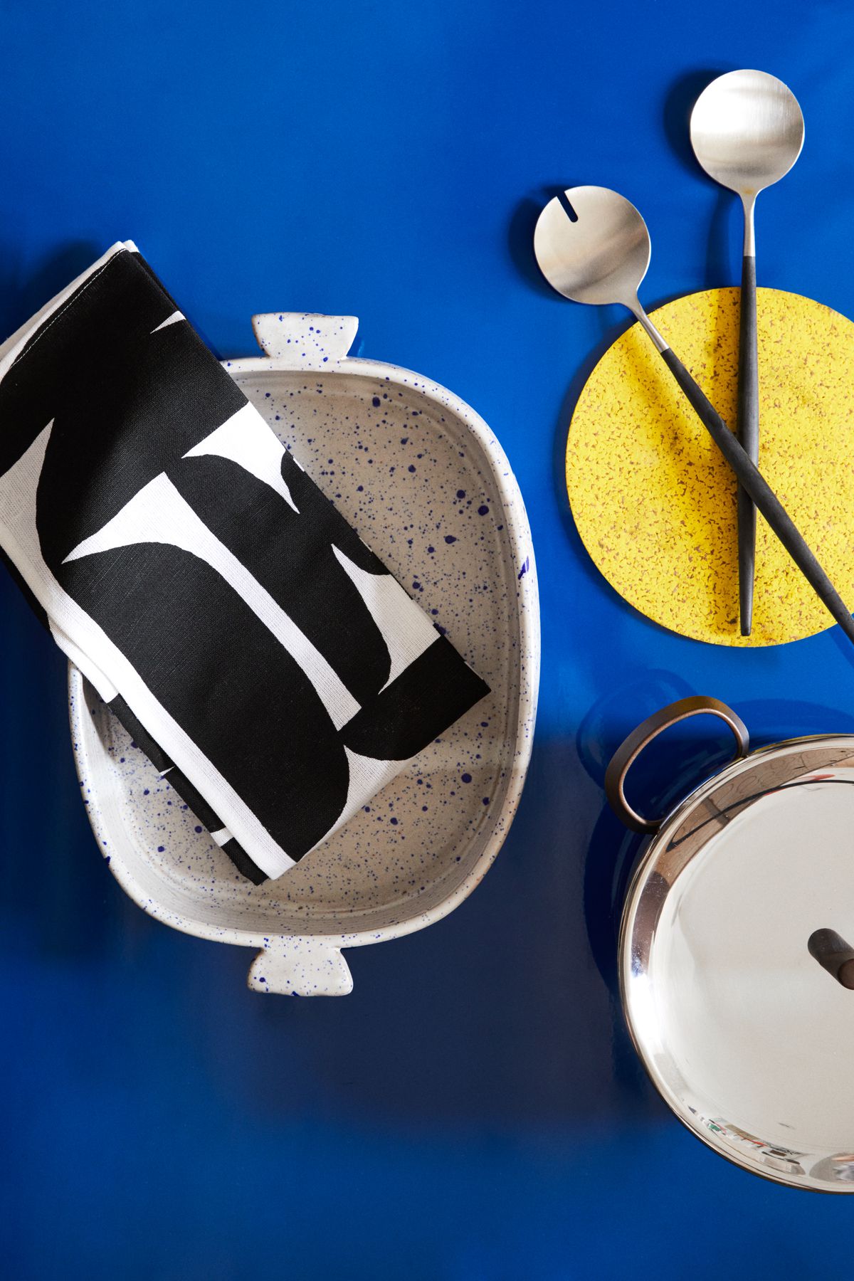 A group of kitchen items including a casserole dish, tea towels, and cookware on a flat blue surface.