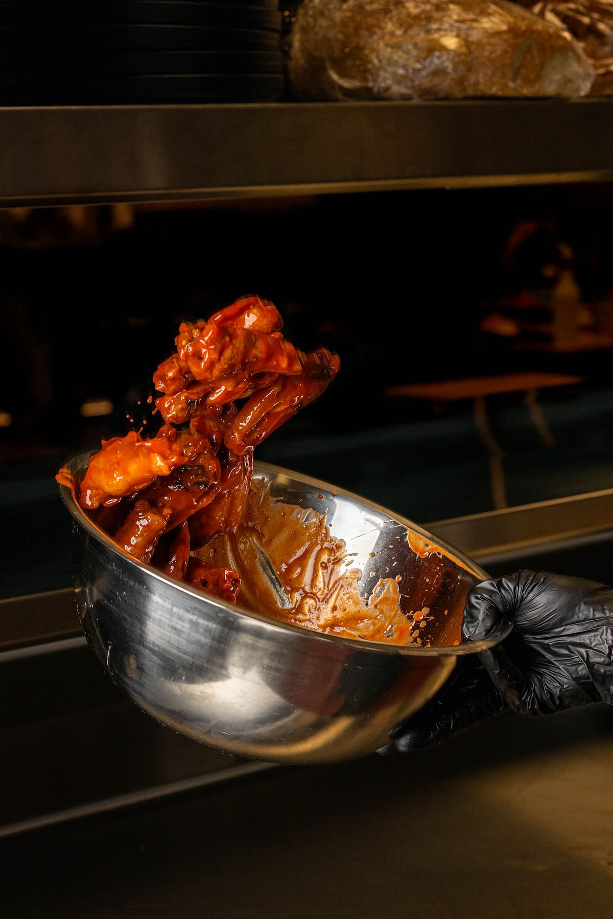 A chef tosses wings in a sauce with a steel bowl.