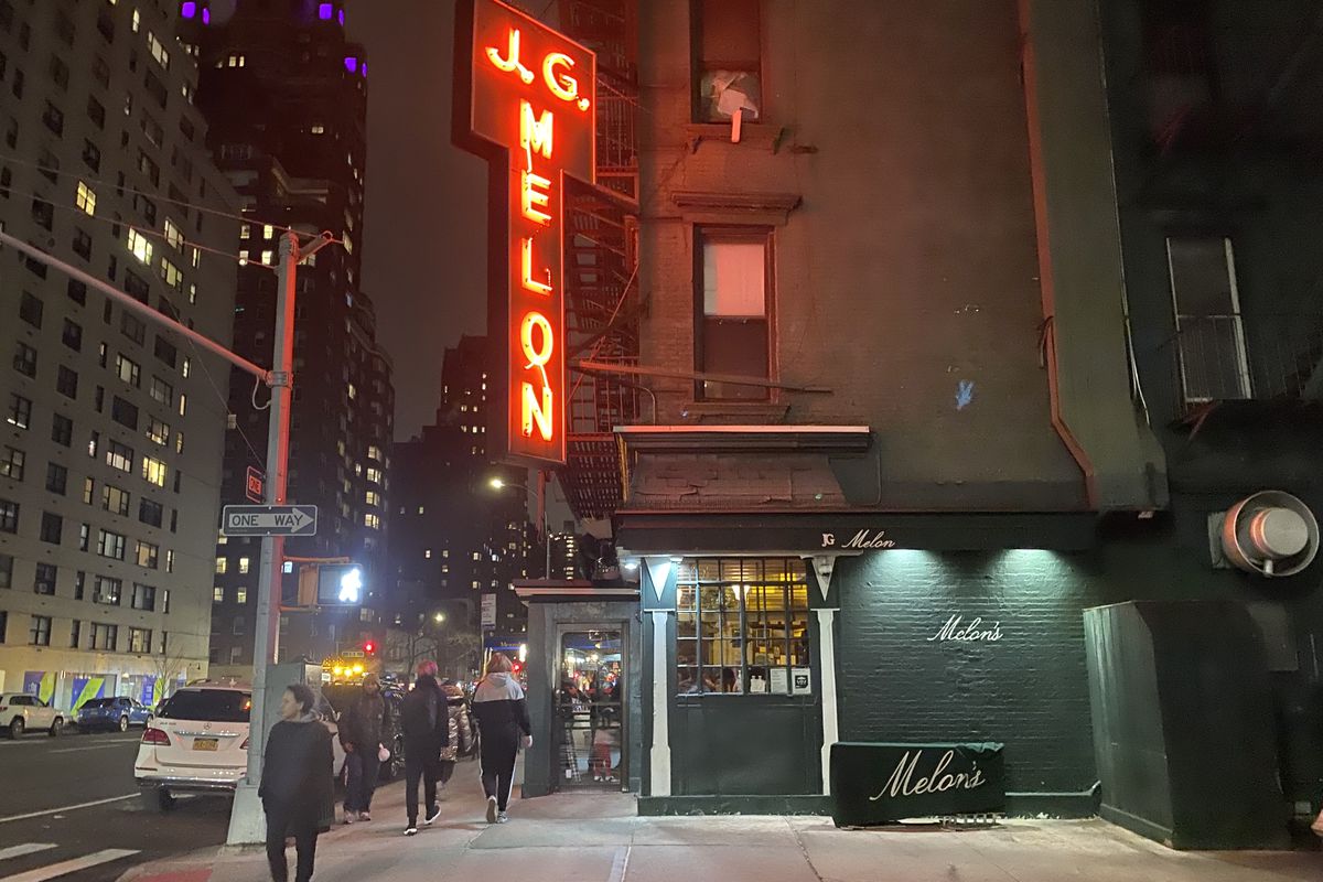 A neon red awning hangs upright outside of J.G. Melon, beckoning patrons inside