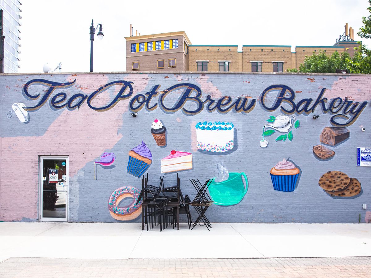 A mural of cakes and cupcakes painted on the side of a brick building.