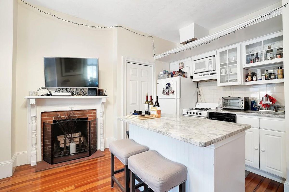 A small, open living room-kitchen area with an island and a fireplace, and lots of cabinetry in the kitchen. 